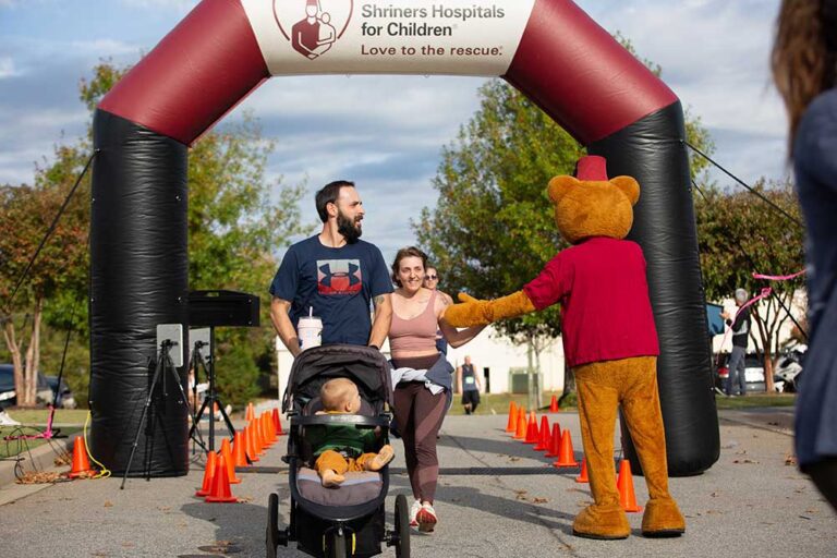 a family pushes a baby in a stroller; Fezzy bear high fives woman